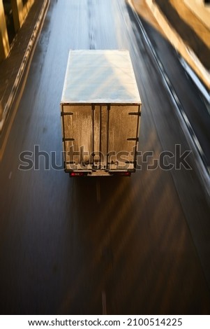 Cargo truck driving on a highway, aerial view. Back view of delivery van in motion. Dirty truck moving on speedway with motion blur effect.