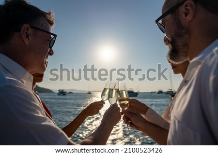 Group of man and woman friends enjoy party drinking champagne with talking together while catamaran boat sailing at summer sunset. Male and female relax outdoor lifestyle on tropical travel vacation Royalty-Free Stock Photo #2100523426