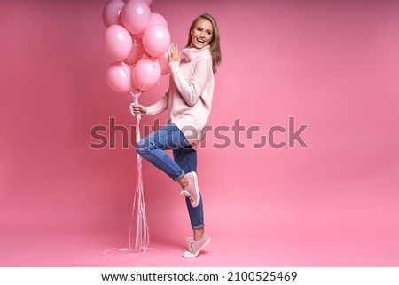 Full length image of beautiful caucasian woman of thirties holding pink balloons