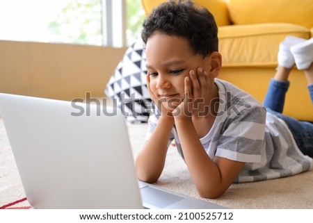 Little African-American boy with laptop watching cartoons on floor at home