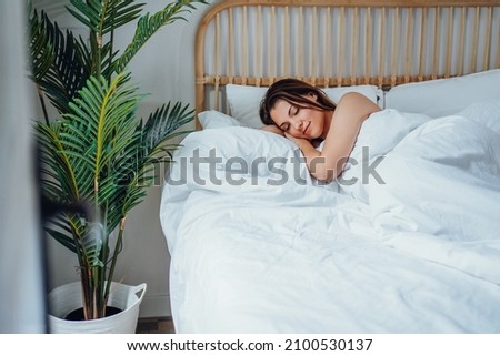 Young calm woman sleeping well alone in comfortable bed. Lady with happy face and smile in light cozy bedroom. Healthy resting in morning, enjoying dreaming. High quality photo