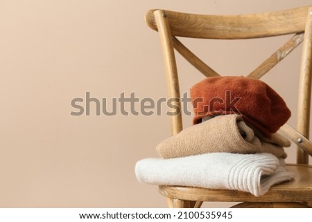 Stylish winter clothes on chair against light background
