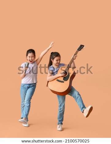 Funny little sisters with guitar and microphone on color background Royalty-Free Stock Photo #2100570025