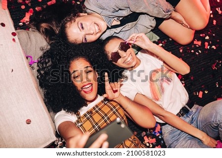Making memories with crazy selfies. Overhead view of three happy friends taking a selfie while lying on the floor at a house party. Group of cheerful female friends having fun together on the weekend.