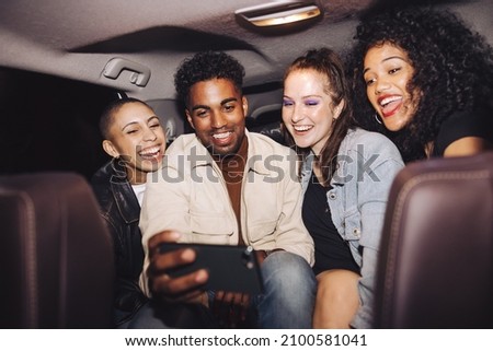 Happy friends taking a selfie together inside a car at night. Group of young friends smiling cheerfully while posing for a group photo. Carefree friends taking a ride home after a party.