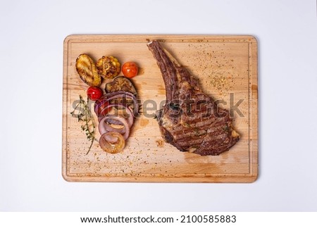 juicy steak on a bone with fried vegetables and fresh onions on a wooden board. isolate