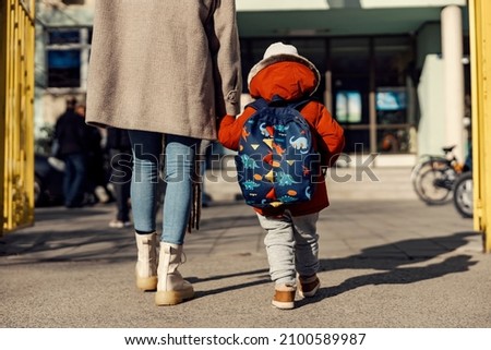 A mother entering the kindergarten yard with her preschooler boy. Royalty-Free Stock Photo #2100589987