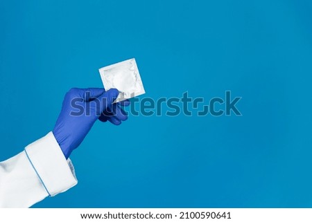 Doctors hand in a glove holds a condom on a blue background with copy space.
