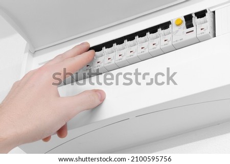 Detail of opened home white fuse box with set of black electric fuses. Male hand in position to switch a fuse off. Electricity and safety. Royalty-Free Stock Photo #2100595756