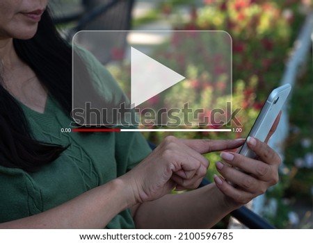 A woman is streaming online, seeing videos on the internet, or attending a live performance, show, or instruction on her mobile phone. Online live streaming video marketing concept, Royalty-Free Stock Photo #2100596785
