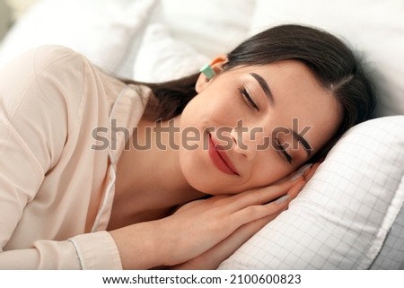 Pretty young woman with blue ear plug sleeping in bed Royalty-Free Stock Photo #2100600823
