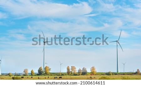 Electric wind farm, a renewable ecological energy source. Horse enclosure, pasture and wind turbines, unique view. Autumn landscape, beautiful and interesting perspective. Royalty-Free Stock Photo #2100614611