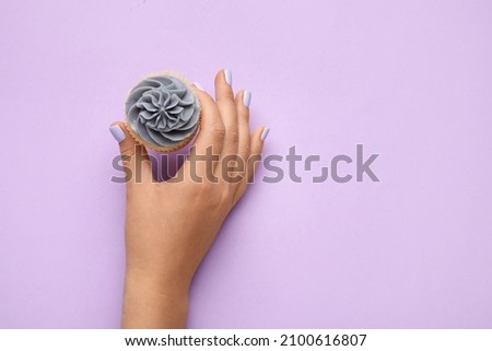 Woman with beautiful manicure holding cupcake on purple background