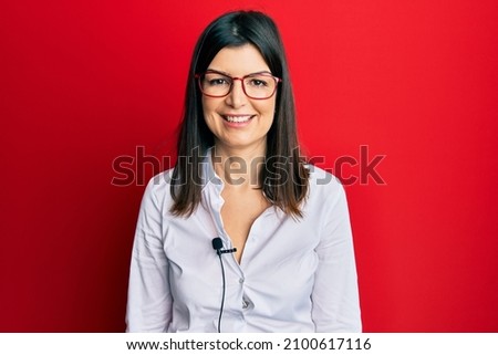 Young hispanic woman using lavalier microphone looking positive and happy standing and smiling with a confident smile showing teeth 