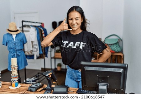 Young hispanic woman working as staff at retail boutique smiling doing phone gesture with hand and fingers like talking on the telephone. communicating concepts. 