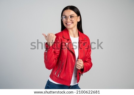 Portrait of woman pointing finger and palm at empty space, looking away with happy smile. Indoor studio shot isolated on grey background 