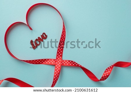 Top view photo of valentine's day decorations inscription love in red silk ribbon heart on isolated pastel blue background with blank space