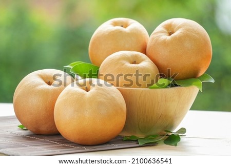 Snow pear fruit in wooden basket, Fresh Nashi pear or Korean pear fruit in the basket over green natural Blur background. Royalty-Free Stock Photo #2100636541
