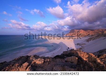 Beautiful sunset on Socotra island with calm beach with no people, soft pink sand and clouds, brown rocks, blue sea. Active travel in Socotra island, protected by Unesco. Yemen. 