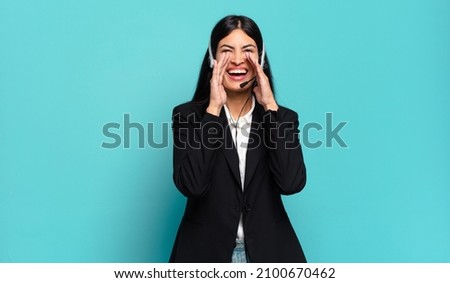 young hispanic telemarketer woman feeling happy, excited and positive, giving a big shout out with hands next to mouth, calling out