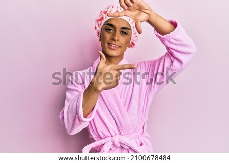 Hispanic man wearing make up wearing shower towel cap and bathrobe smiling making frame with hands and fingers with happy face. creativity and photography concept. 