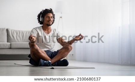 Meditation Practice. Relaxed Black Man Meditating At Home In Lotus Position, Smiling African American Guy Wearing Wireless Headphones Sitting With Closed Eyes On Yoga Mat, Panorama With Copy Space Royalty-Free Stock Photo #2100680137