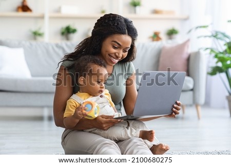 Happy Black Mother And Her Little Infant Son Using Laptop Computer At Home, Smiling African American Mom Showing Cartoons To Toddler Child While Relaxing On Floor In Living Room Together, Free Space