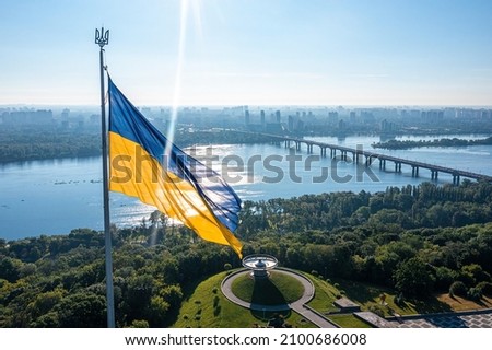 Aerial view of the Ukrainian flag waving in the wind against the city of Kyiv, Ukraine near the famous statue of Motherland. Royalty-Free Stock Photo #2100686008