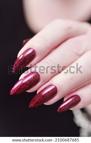 Female hands with long nails and burgundy manicure holding a bottle of nail polish