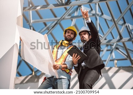 Civil engineer and construction worker manager holding digital tablet and blueprints ,They are looking to next construction phase, cooperation teamwork concept. Royalty-Free Stock Photo #2100709954