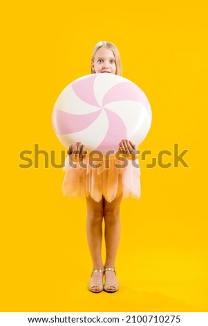 Christmas sweetness. A cute girl is holding a huge pink and white candy on a yellow background. Sweet gift. Large lollipop.