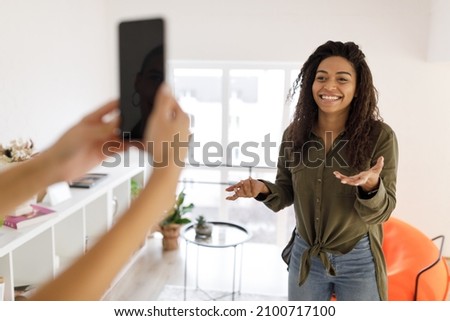 Blogging Concept. Smiling black female influencer recording lifestyle blog talking to camera, her friend filming video holding mobile phone at home. Happy young lady shooting vlog for her channel