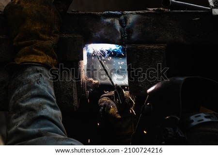 a welder in a protective mask welds iron structures in a factory