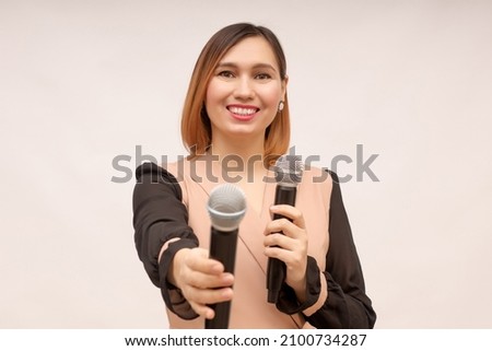 A young woman stands on a white background with a microphone in her hands and invites to speak or sing together while giving a second microphone