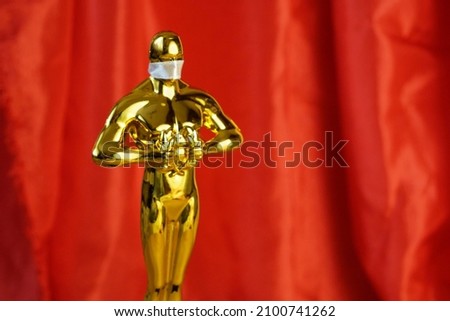 Hollywood Golden Oscar Academy award statue in medical mask on red background with copy space. Success and victory concept. Oscar ceremony in covid-19 time