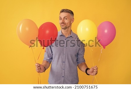 smiling handsome man hold balloons on yellow background, holiday.