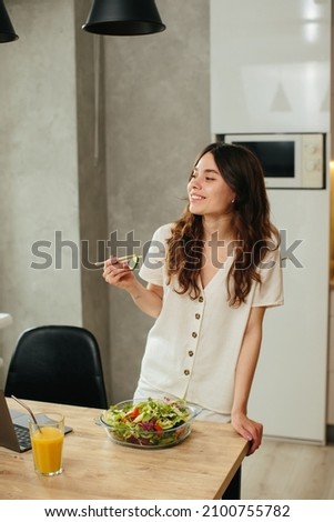 Young woman eating salad while sitting in kitchen - stock photo
