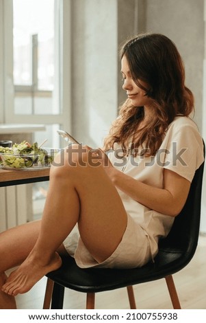 Woman eating salad while sitting by laptop in kitchen - stock photo
