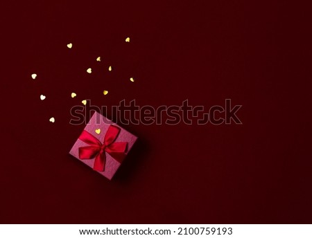 Red gift box with bow and confetti on a red background. Valentines day gift flat lay with gold glitter and space for text