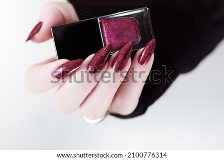 Female hands with long nails and burgundy manicure holding a bottle of nail polish