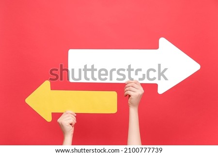 Close up of female hands holding two paper arrow pointing left and right, isolated on red color background studio with copy space for your text or design. Business vision, choice, achievement concept Royalty-Free Stock Photo #2100777739
