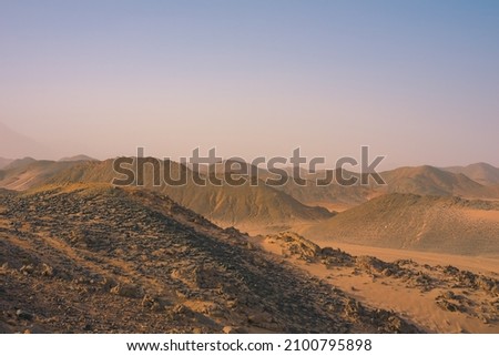 Safari and travel to Africa, extreme adventures or science expedition in a stone desert. Sahara desert at sunrise, mountain landscape with dust on skyline, hills and traces of the off-road car.