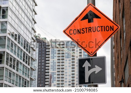 Construction orange sign near construction site against tall buildings