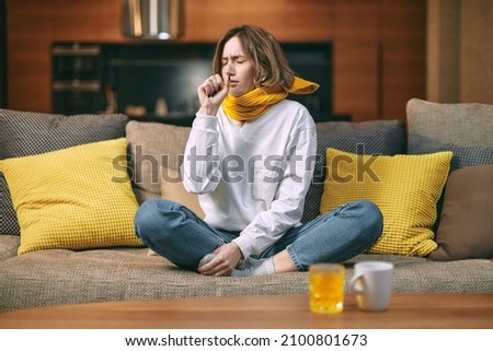 Cold ,flu cough. Sick woman coughing sitting on sofa at home with cup of hot drink, glass of medication with vitamin c Royalty-Free Stock Photo #2100801673