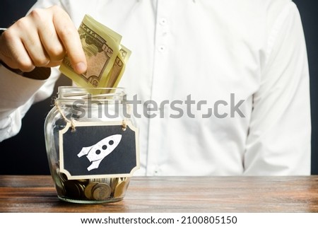 A man puts money into a startup jar. Research and development. Crowdfunding. Fundraising, financing with investment in promising projects and ideas. Entrepreneurship. Saving on a flight into space Royalty-Free Stock Photo #2100805150