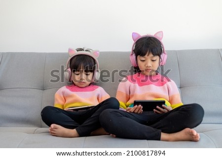 Asian siblings girl surfing net social media and playing on smartphone and digital tablet, e-learning at home