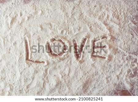 Love written with finger on a flour spread over a kitchen table. Royalty-Free Stock Photo #2100825241