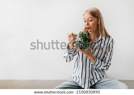 Healthy lifestyle concept. Young blonde woman sitting on the floor, eating salad and smiling
