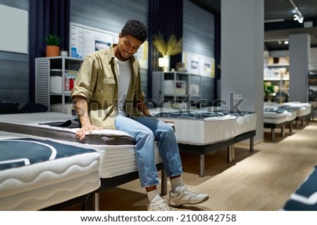 Man choosing mattress sitting on shop bed Royalty-Free Stock Photo #2100842758