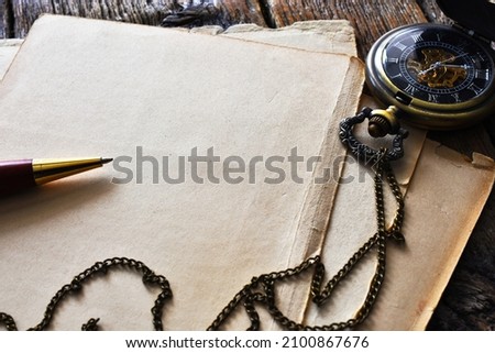 A top view image of an old vintage pocket watch and pen on old vintage stationary.  